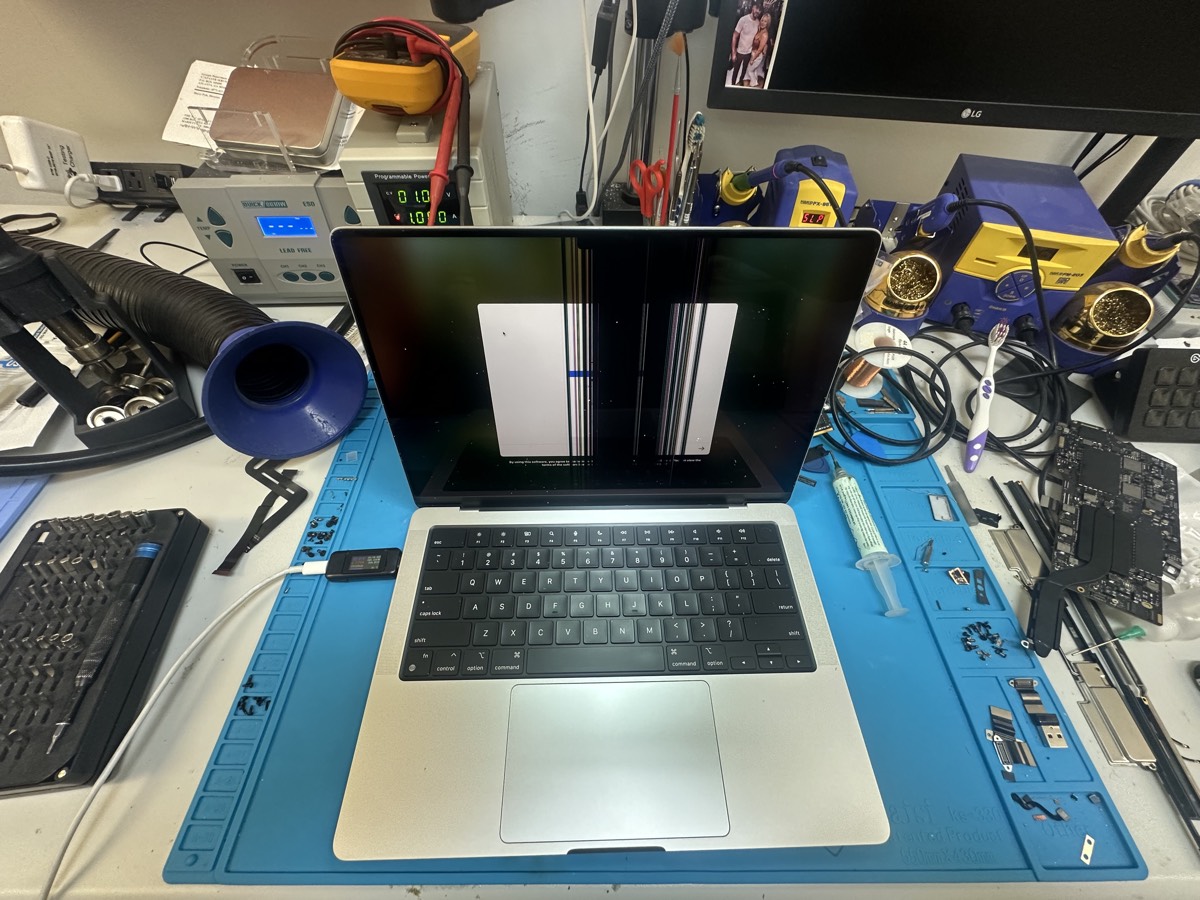 MacBook Pro with cracked display on blue repair mat surrounded by professional repair tools